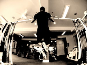 A view from the ground of a guy performing pull-ups with his chest at the bar. 