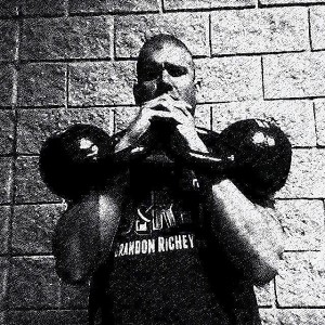 Black and white image of Brandon holding a pair of kettlebells in the rack position. 