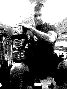 Black and white image of a man sitting on the edge of a bench about to perform a single arm dumbbell press with 90 lbs. 