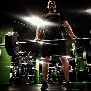 Brandon standing in the lockout position deadlifting 315 lbs. with the barbell. 