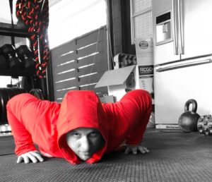 Man in a red hoodie performing push-ups while looking straight ahead at the camera. 
