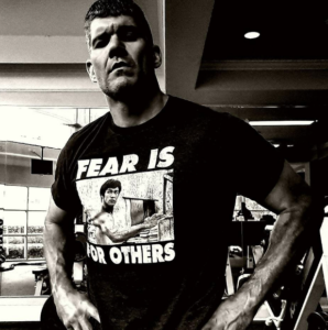 Black and white image of Brandon standing displaying a Bruce Lee shirt. 