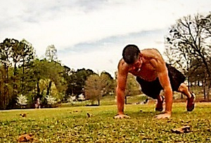 Lean muscular man performing push-ups in a field. 