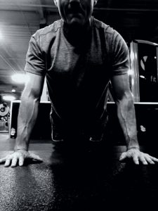 Black and white image of a man doing the cobra stretch coming out of the Yoga downward dog pose. 