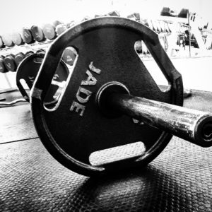 A barbell on the floor showing one end with a 45lb. plate in the forefront of the image. 