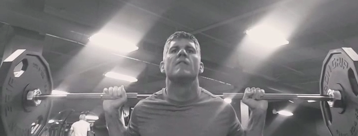 Black and white image showing a barbell on Brandon's shoulders prior to squatting. 