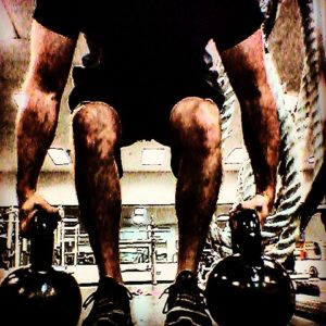 A man bending to grab a pair of kettlebells off the ground in a suitcase deadlift movement. 