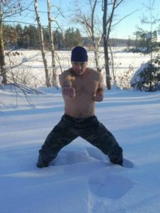 A shirtless man shadowing boxing knee deep in the snow. 