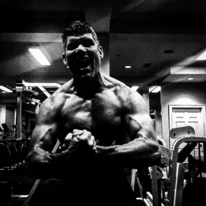 Black and white image of a muscular man flexing and posing down the camera. 