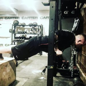 Man performing a push-up on suspension rings with his feet elevated on a plyo-box. 