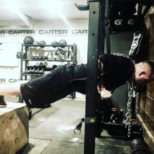 Man performing a suspension push-up with his hands locked in suspension straps and his feet elevated on a plyo-box. 