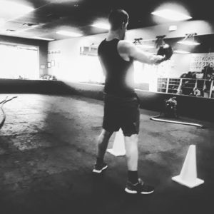 Black and white image of a trainee performing the kettlebell swing with his back to the camera. 