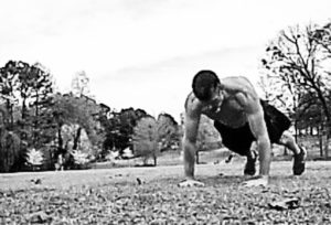 Black and white image of Brandon performing push-ups outdoors in the middle of a field. 