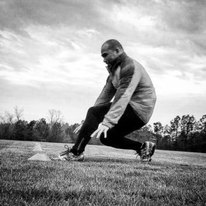 Black and white image of a man performing sprint drills decelerating at a cone. 