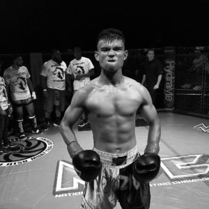 Black and white image of a fighter flexing and showing his "fight face" prior to a Thai boxing match. 