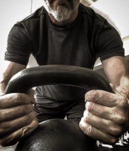 Man holding a kettlebell by the sides of the handle in front of the camera.  