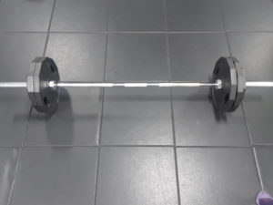 Black and white photo including a barbell with 225 lbs of weight setting on the floor. 