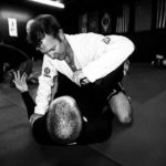 Black and white image of a man in white rolling over a man in black during Jiu Jitsu. 