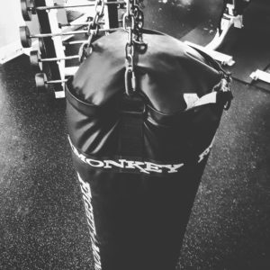 A black and white image of a long punching and kicking bag that is torn at the top. 