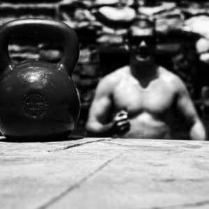 Black and white photo with a kettlebell in the foreground with Brandon in the background. 