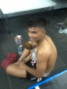 Fighter sitting on the ground holding a white bottle of CobraZol Sport smiling after a fight! 