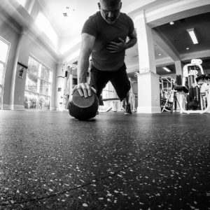 Black and white image of Brandon performing a one arm push-up off of a kettlebell. 