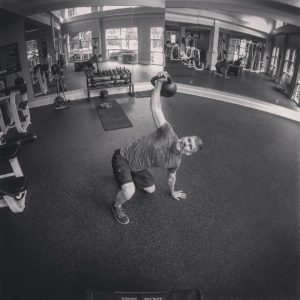 Black and white image of a man halfway through the turkish get up lifting with his right arm. 