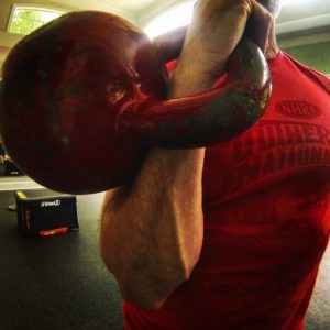 Man holding a big red kettlebell in the racked position with his right arm. 