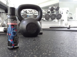 Bottle of CobraZol Sport setting on the ground in front of a kettlebell. 